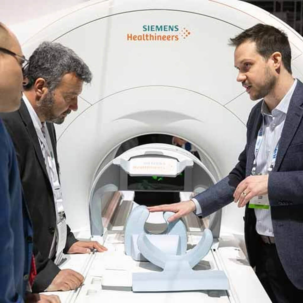Two professionals discussing medical imaging technology beside a Siemens MRI scanner at a healthcare conference or exhibition
