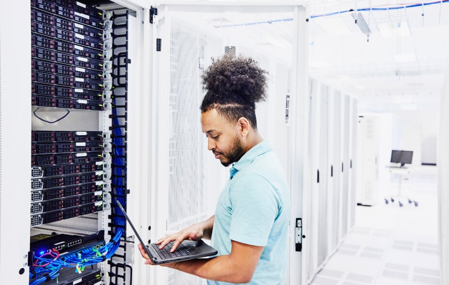 An IT team member is holding an open laptop connected to hardware for on-premises data storage.