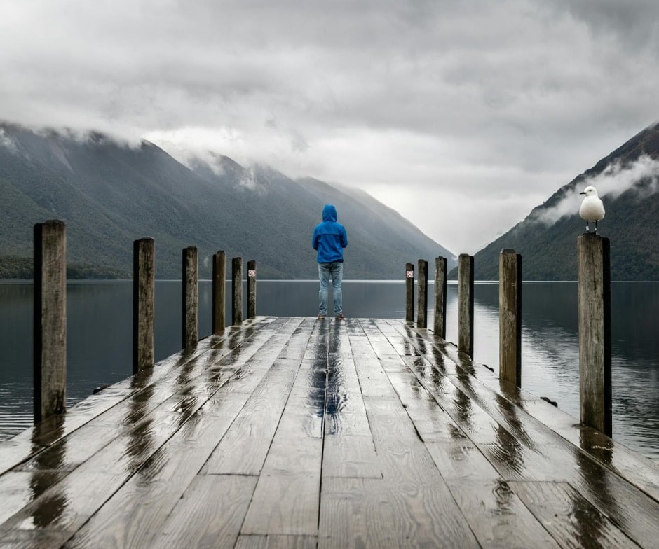 person at the edge of pier and looking at water and mountains
