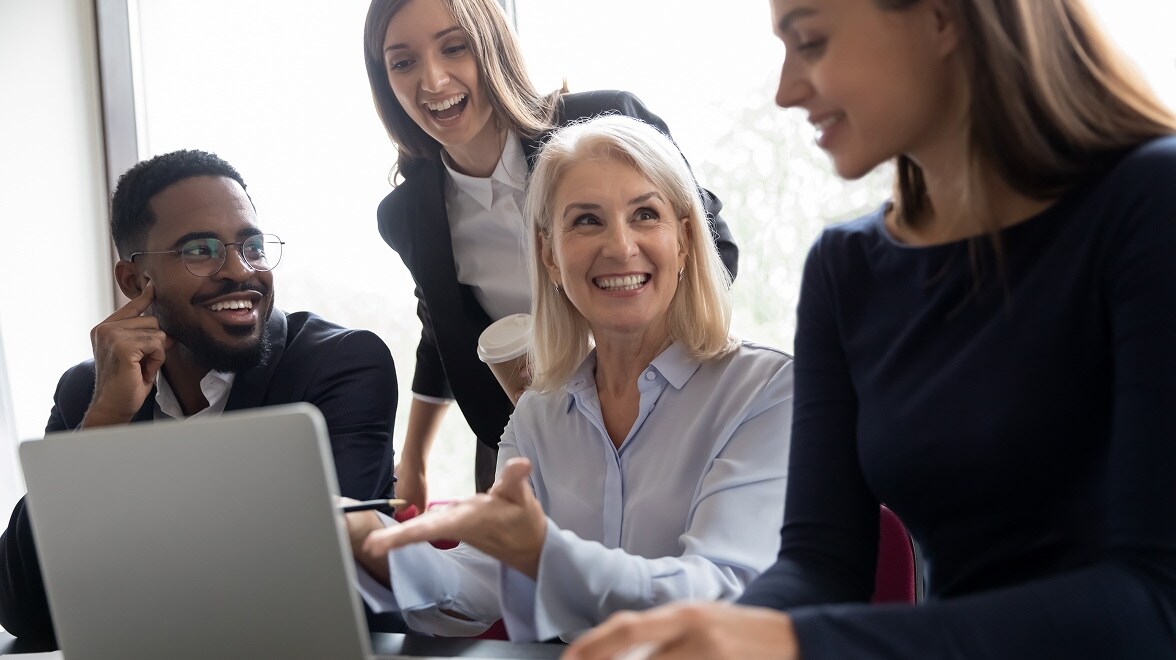 Profesionales reunidos alrededor de un portátil sonriendo