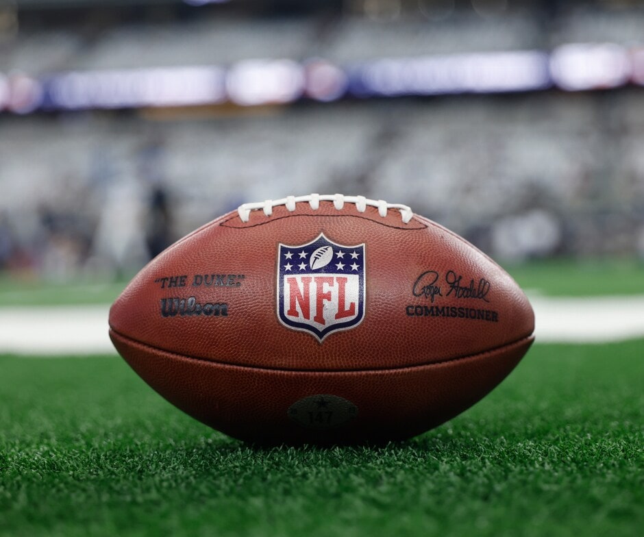 Primer plano de un balón de fútbol americano de la NFL descansando en el campo con el logo de la NFL bien visible.