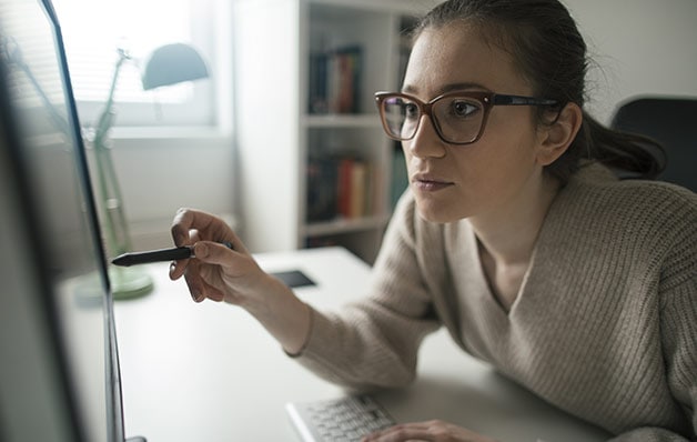 woman with glasses using a pen as a pointer towards her monitor