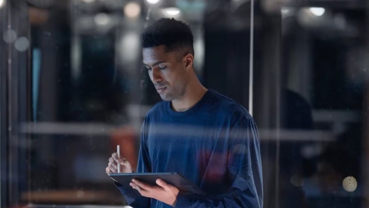 Une personne se tient dans l'allée d'un data center et travaille avec des équipements devant de grands racks de serveurs.