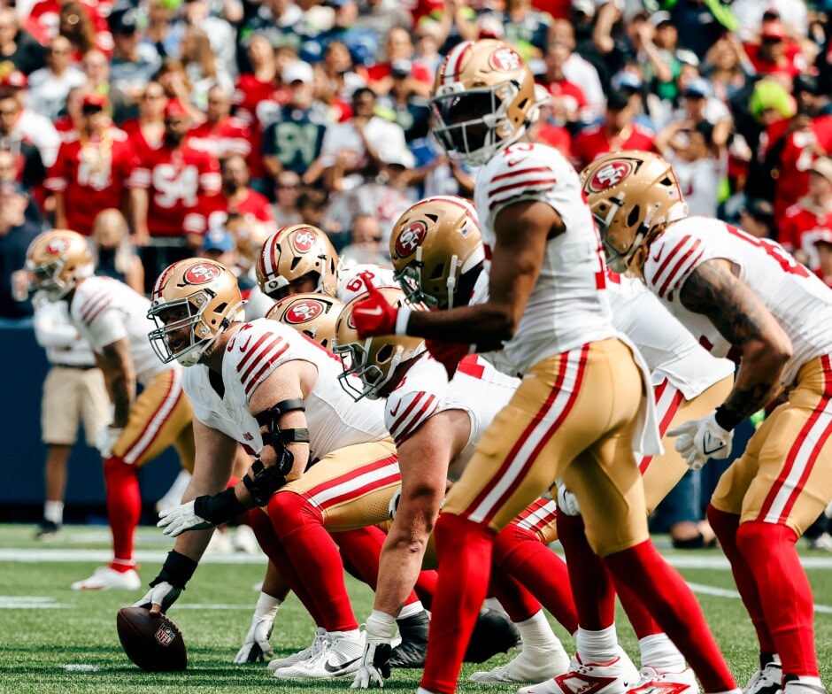Jugadores de San Francisco 49ers alineados en la línea de scrimmage durante un partido, preparándose para el snap.