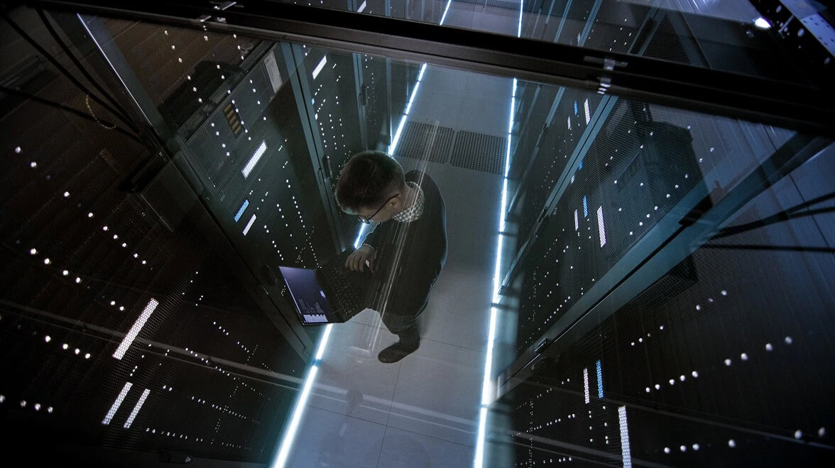 Especialista em TI trabalhando em um corredor de data center cercado por racks de servidores iluminados.