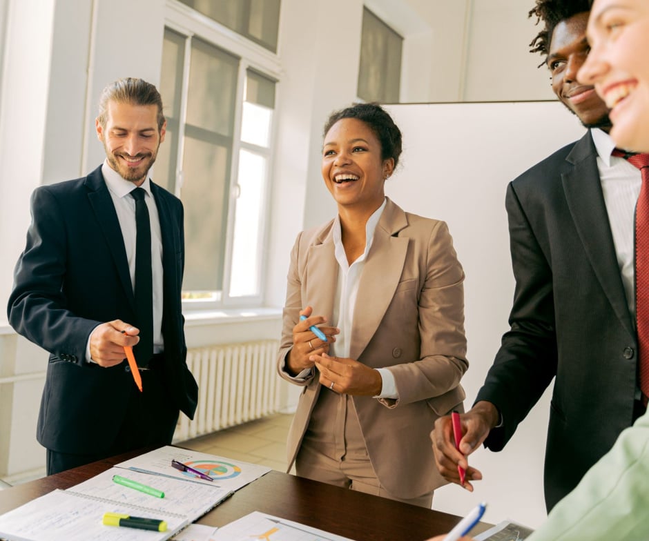 Business professionals gathered around a table reviewing charts and discussing ideas in a bright office setting.