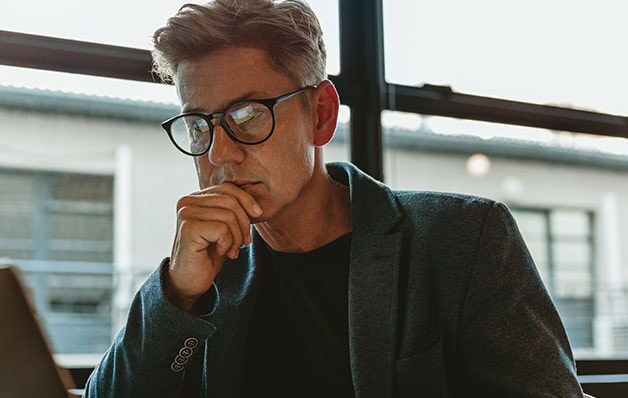man with black glasses looking at laptop pensively