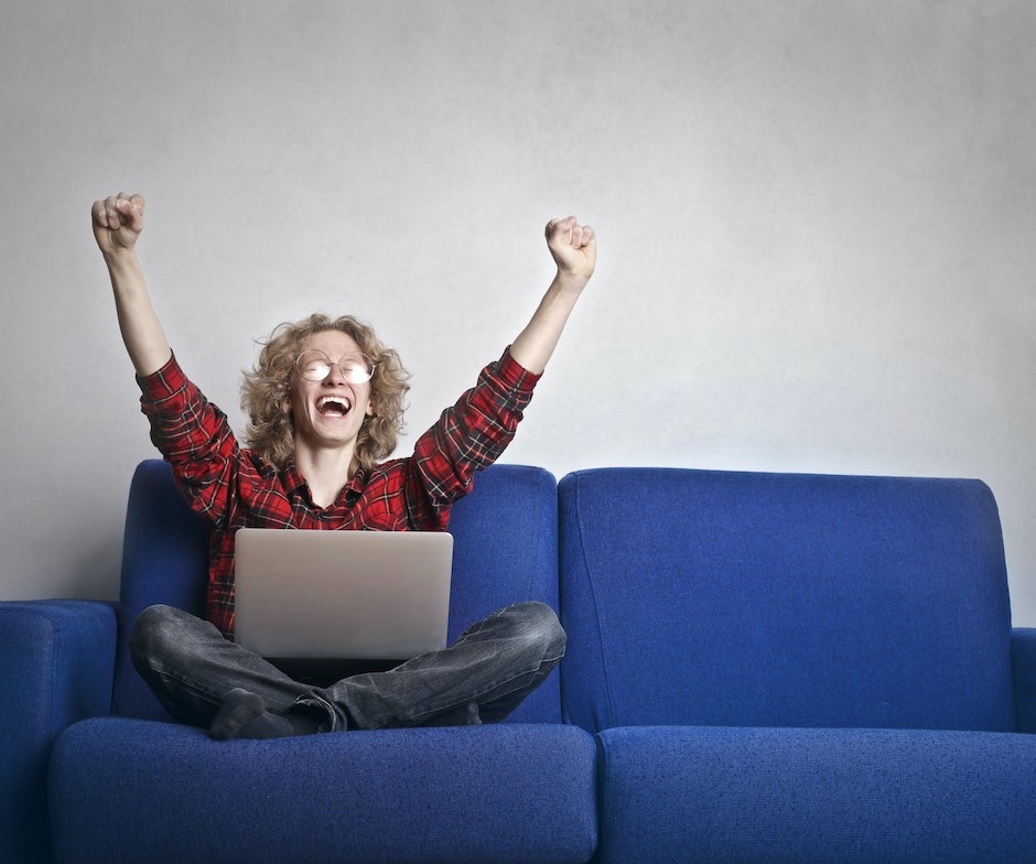 person sitting on blue couch and raising hands happily and laughing