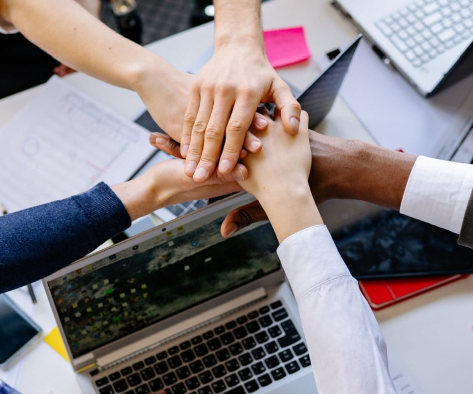 Team members placing their hands together in a gesture of collaboration over a shared workspace