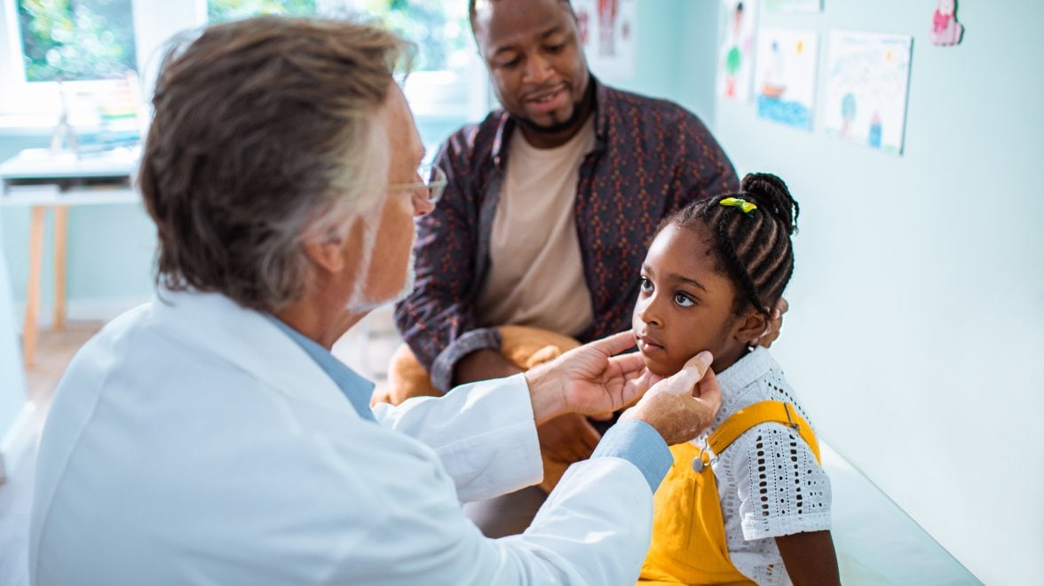 médecin examinant une enfant pendant que son père est assis à côté d'elle sur la table d'examen