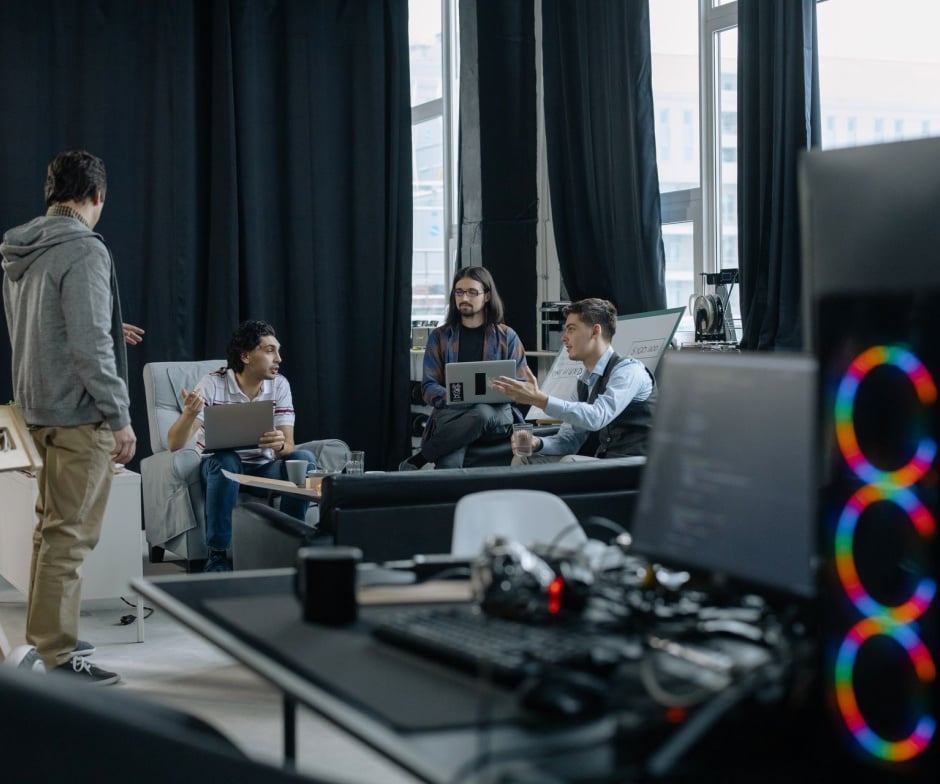 Team members collaborating with laptops in a modern office workspace, with computer equipment visible in the foreground.