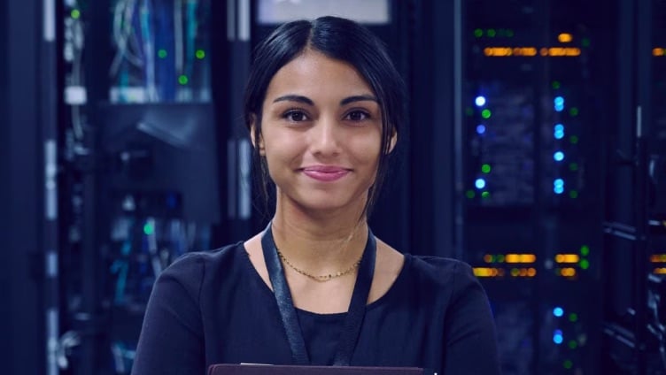 Une personne se tient dans l'allée d'un data center et travaille avec des équipements devant de grands racks de serveurs.