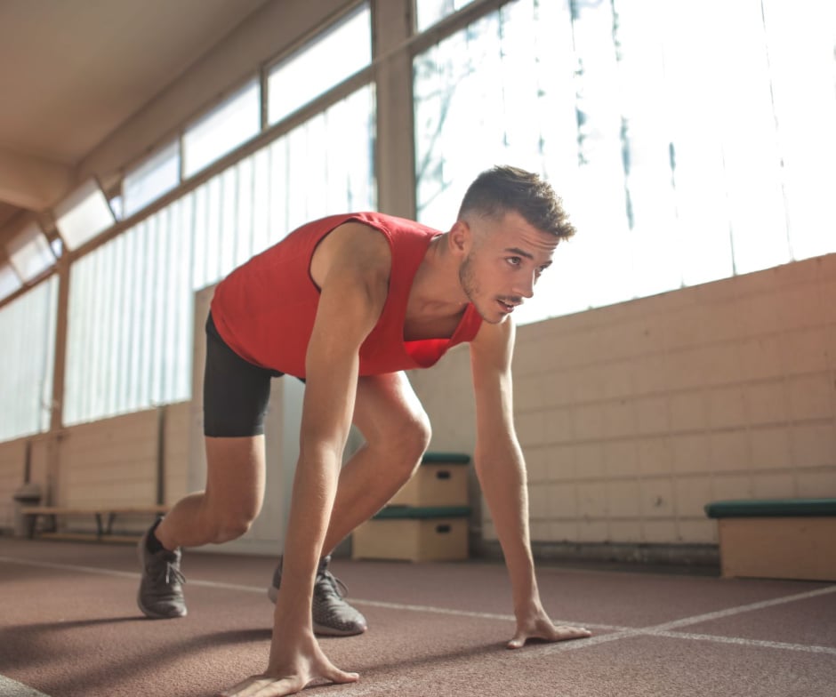 Athlete in starting sprint position on an indoor running track, representing fitness, sports performance, and athletic training.