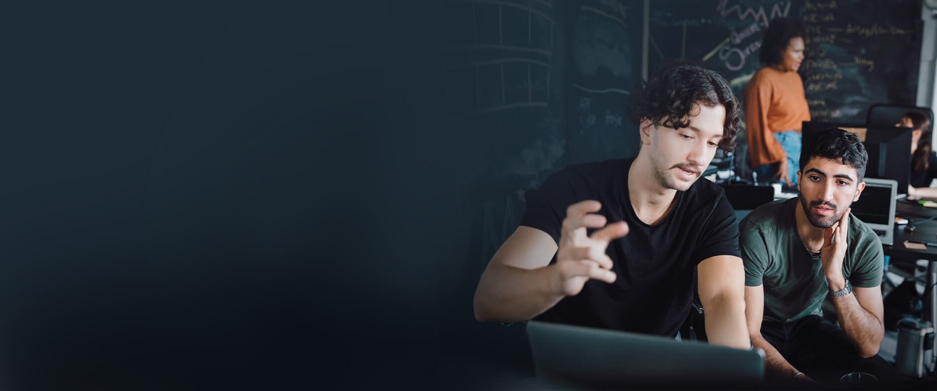 Smiling professional holding a tablet in front of desk with computers