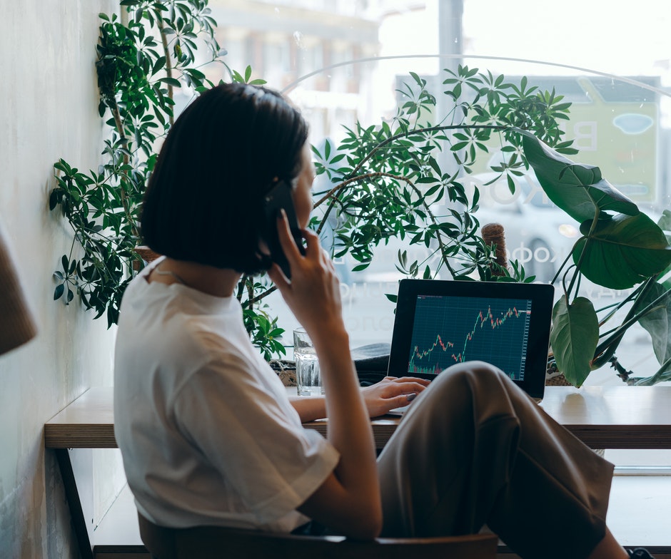woman working on phone and laptop, surrounded by plants
