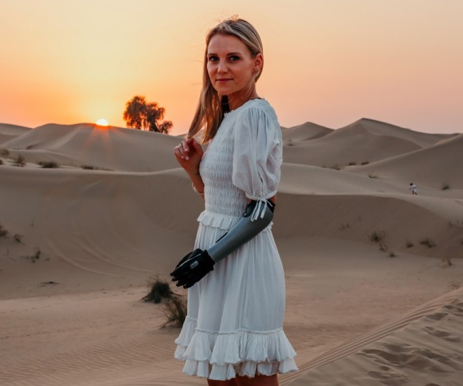 Person in white dress with prosthetic arm with sand dunes in background