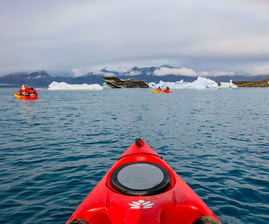 Red kayak on calm water near floating icebergs