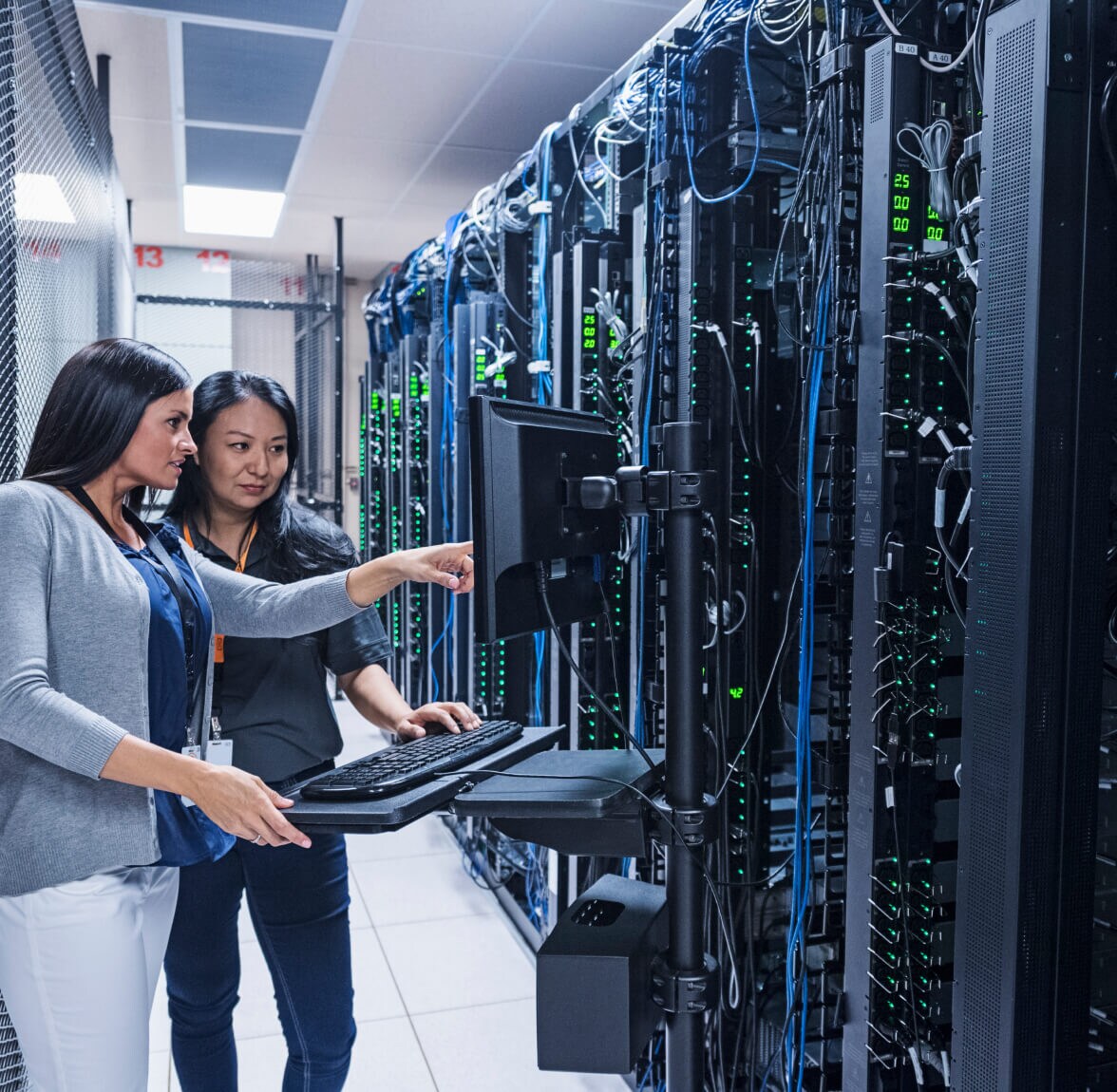 Two IT professionals monitoring servers and reviewing system data in a data center.