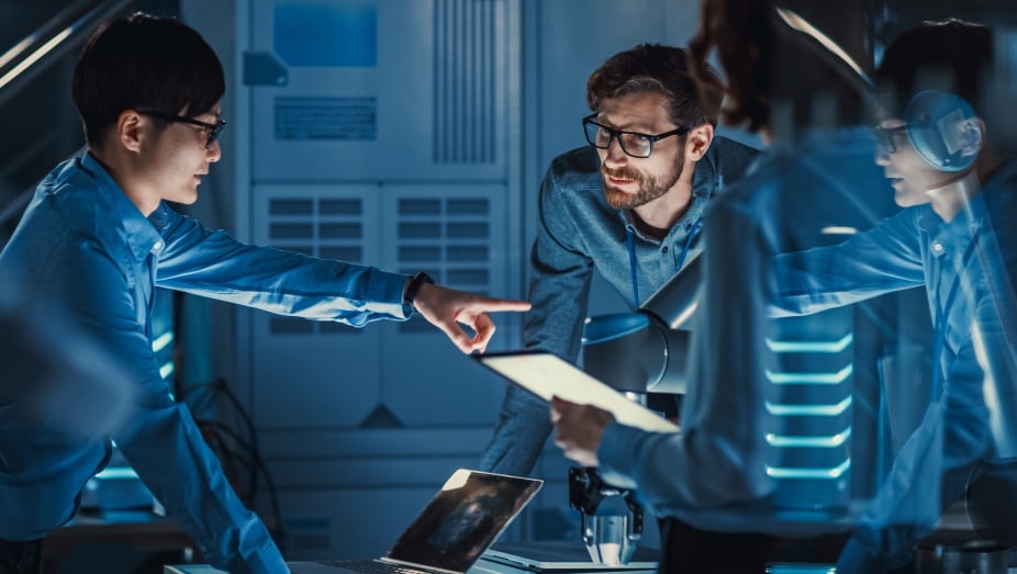 A group of IT professionals with laptops are gathered around a table in an on-prem data environment.