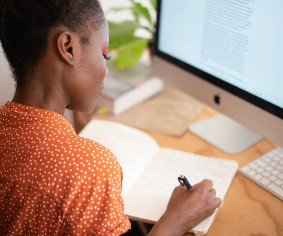 person sitting in front of desktop and writing on notebook