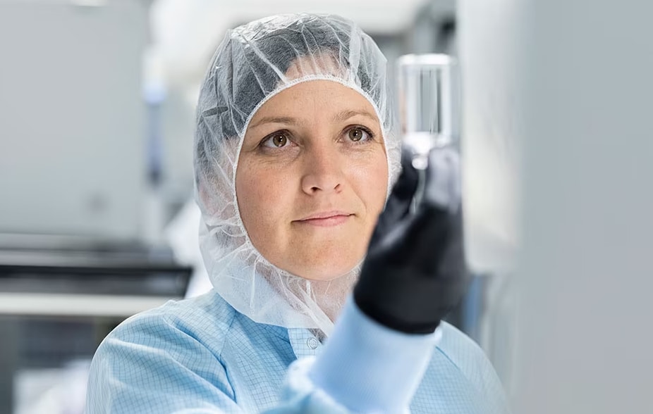 A woman wearing medical scrubs holds up a sample container to inspect its contents.