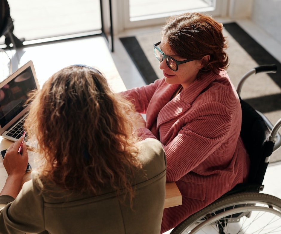 two people sitting on chairs and laptop on table discussing