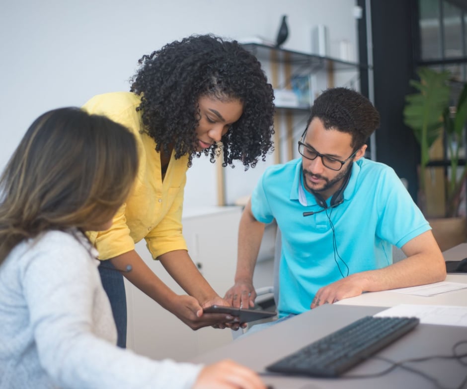 Three coworkers collaborating around a mobile device in an office environment.