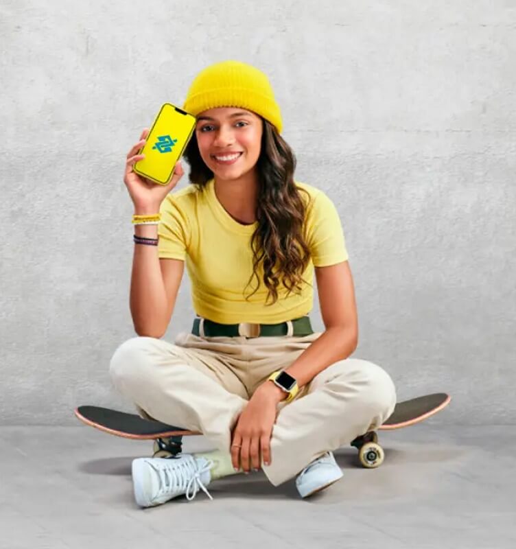 A woman seated on a skateboard holding a mobile phone