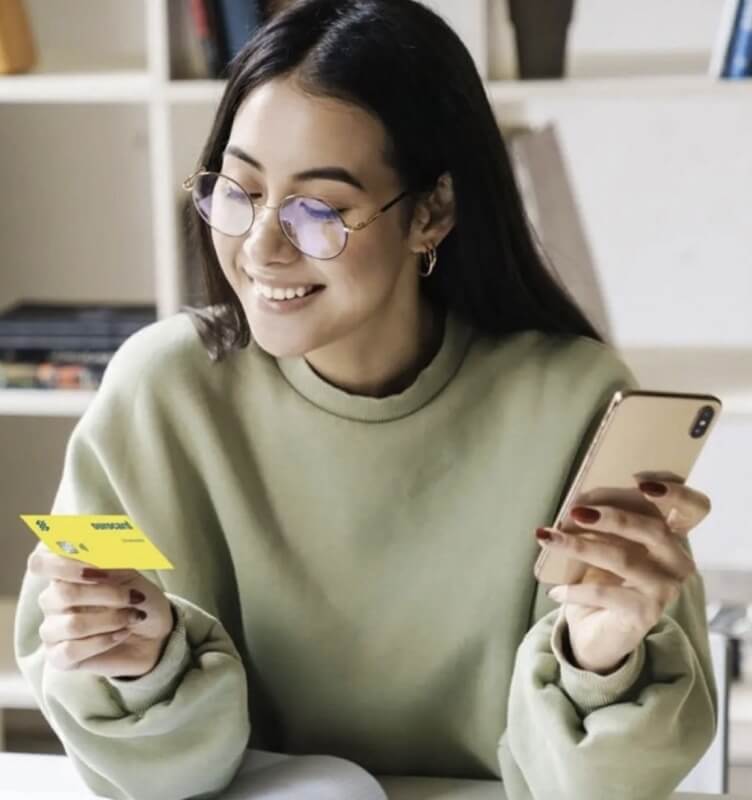 A woman holding a Banco do Brasil card and a mobile phone