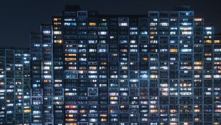 Apartment tower at night with numerous illuminated windows across the building façade.