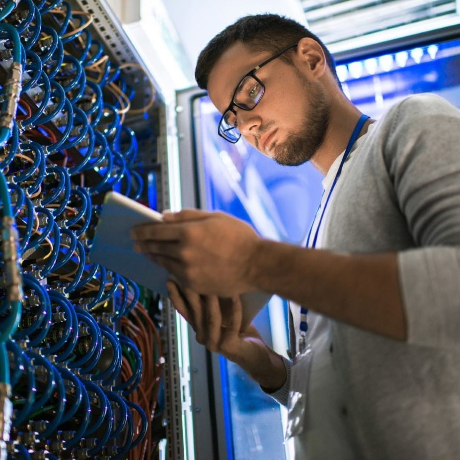 man looking at tablet in front of a wall full of cables