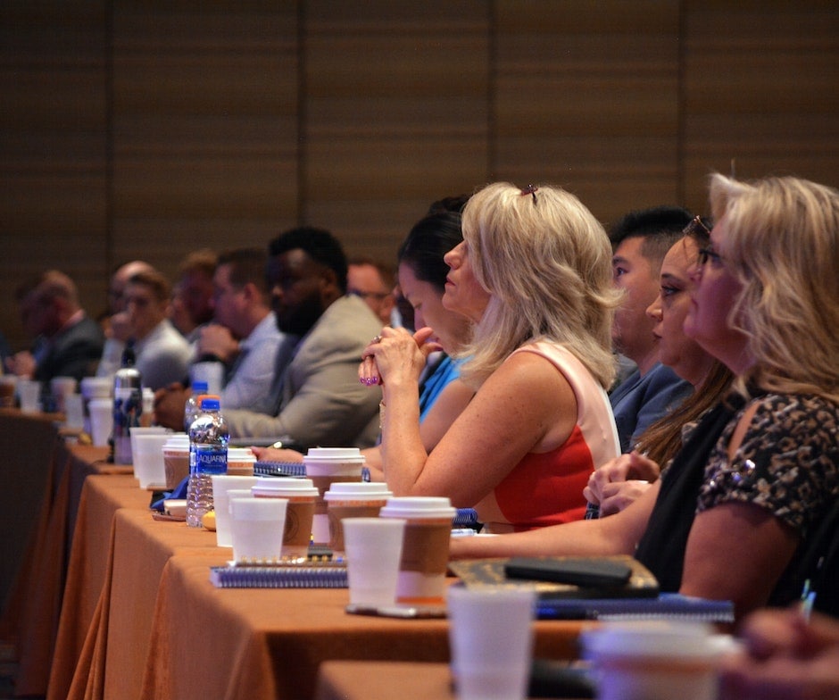 group of people sitting in a conference room listening to the speaker with water glass and coffee on the table